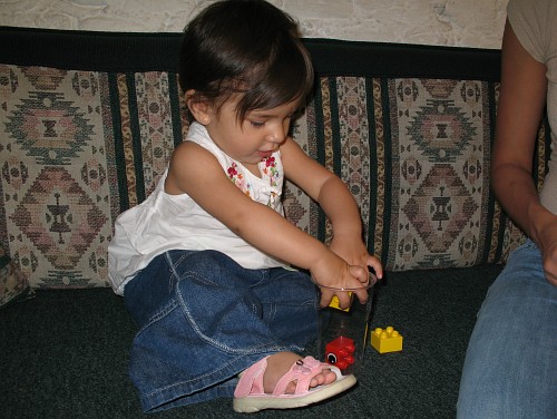 Alice putting the second Duplo brick in the plastic cup.