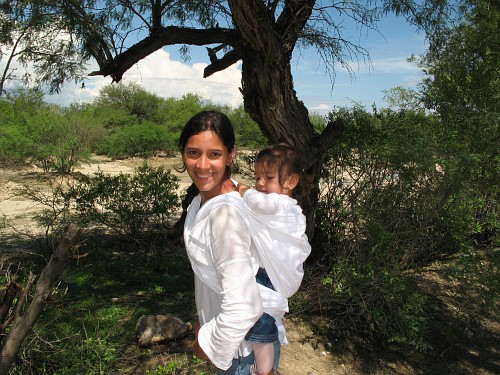 Esme carrying Alice on her back using a makeshift rebozo.